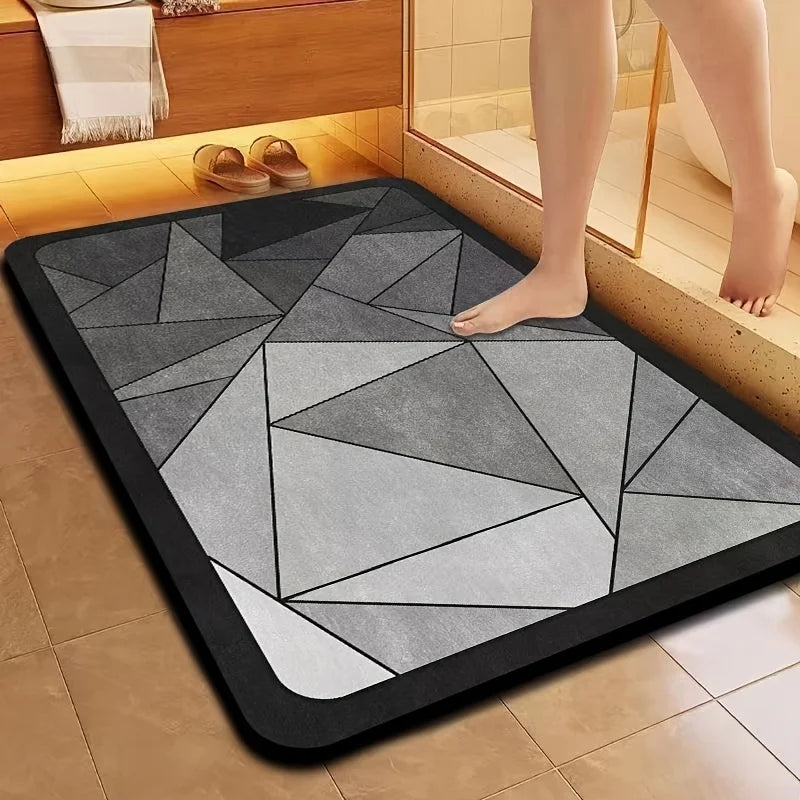 A rectangular gray bath mat with a geometric pattern is placed on a tiled floor next to a bathtub.