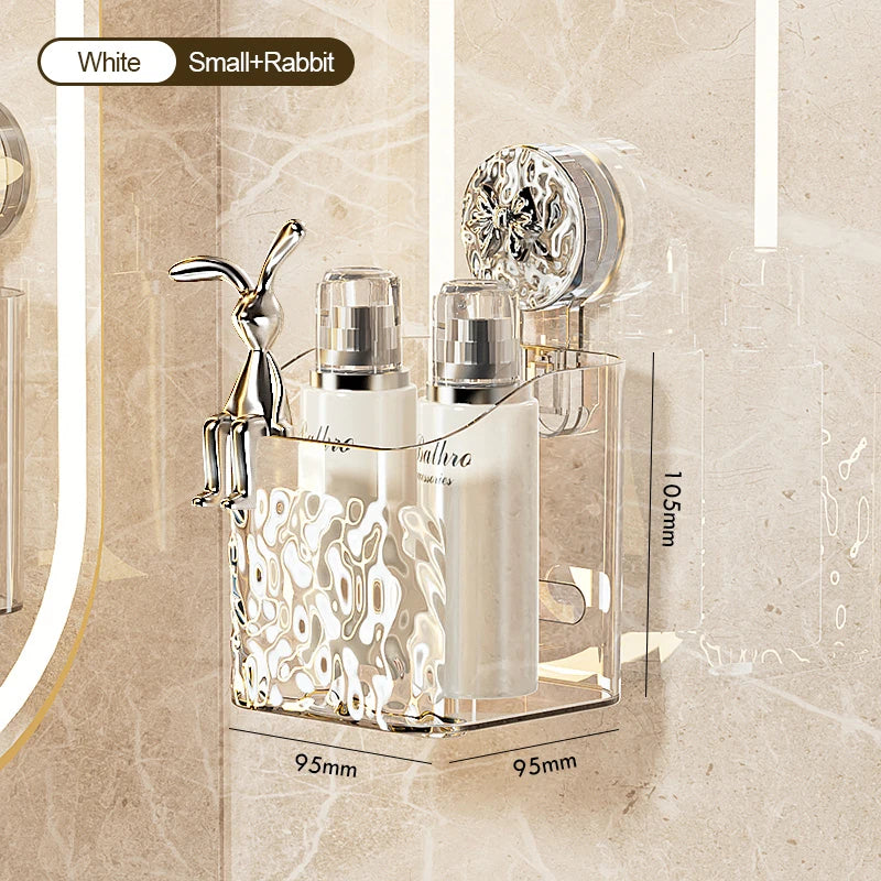 A clear glass storage rack with a stainless steel bunny figurine and two white glass bottles for bathroom products.