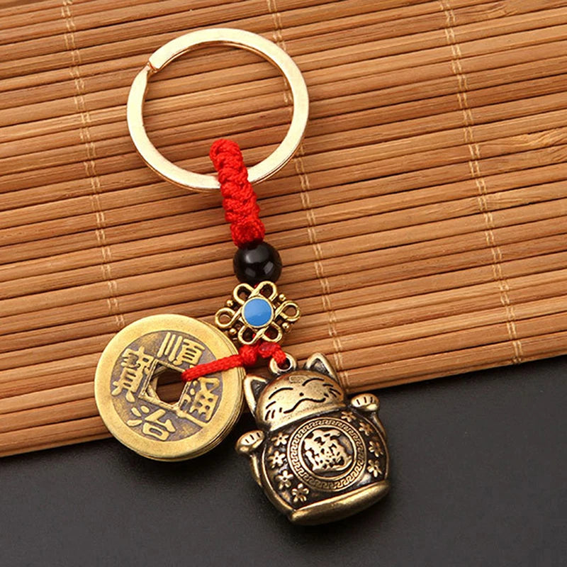 Vintage gold-tone lucky cat keychain with a round coin charm and red tassel on a bamboo mat.