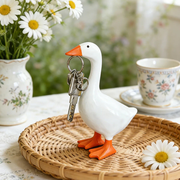 Weiße Gans-Anhänger-Skulptur mit orangem Schnabel auf einem geflochtenen Tablett umgeben von Margeriten.