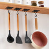 A set of five wooden and black silicone spatulas hanging from a wooden rack on a white wall.