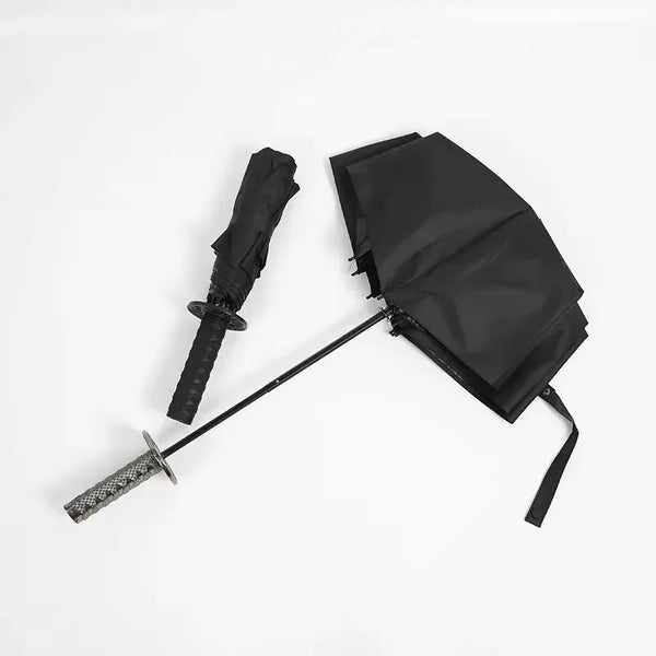 A black folding katana sword umbrella with a black sheath and blade is displayed on a white background.