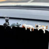 A set of four cute healing cat figurines lined up on a car window sill.