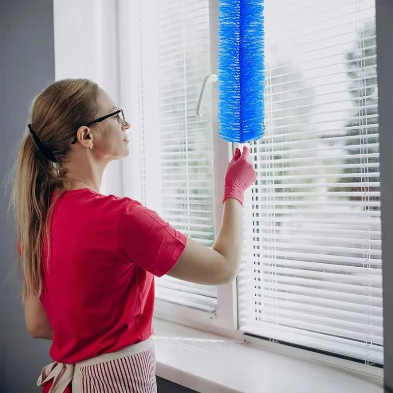 A woman in a red shirt is cleaning horizontal blinds with a blue multifunctional fan and blind cleaning brush.