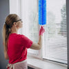 A woman in a red shirt is cleaning horizontal blinds with a blue multifunctional fan and blind cleaning brush.