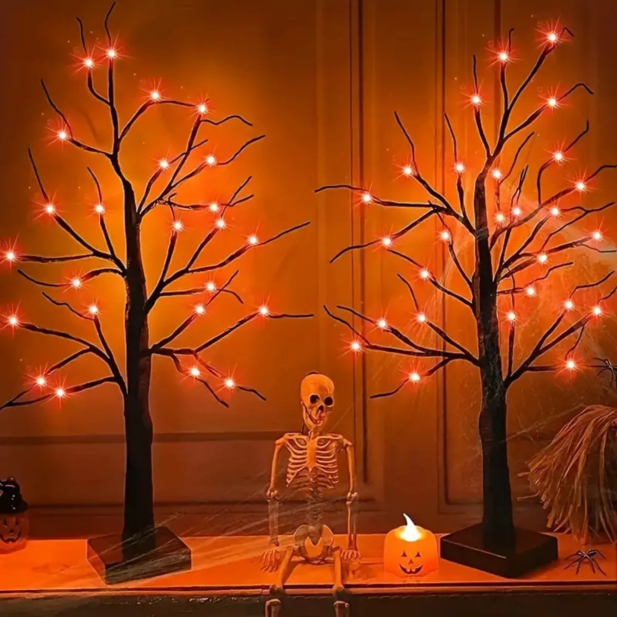 Dekorativer Birkenbaum-Licht mit orange- und lila LED-Lichter neben einem Skelett und einer Laterne.