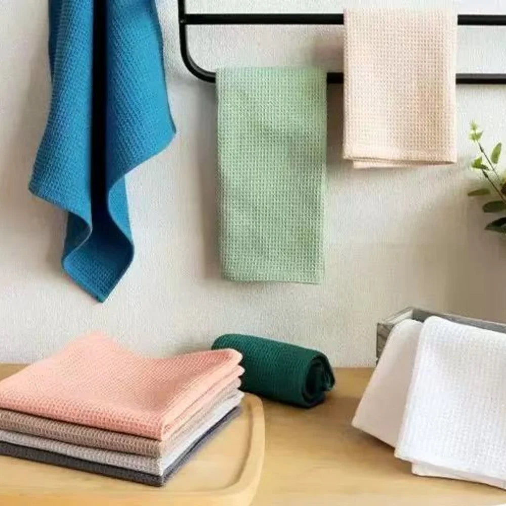A collection of light green and pink waffle weave towels are displayed on a wooden surface.