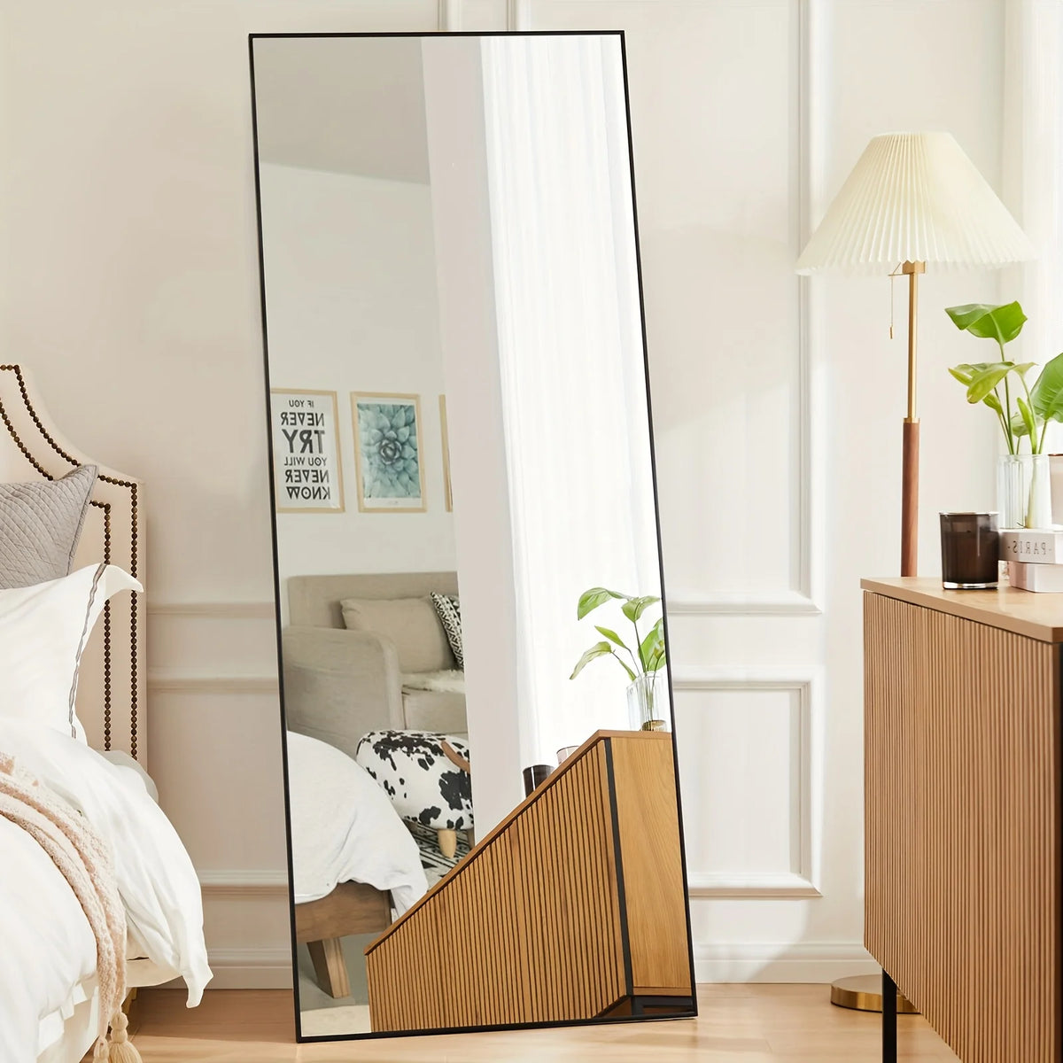 A full length arch mirror with a black frame reflects a bright interior and a potted plant.