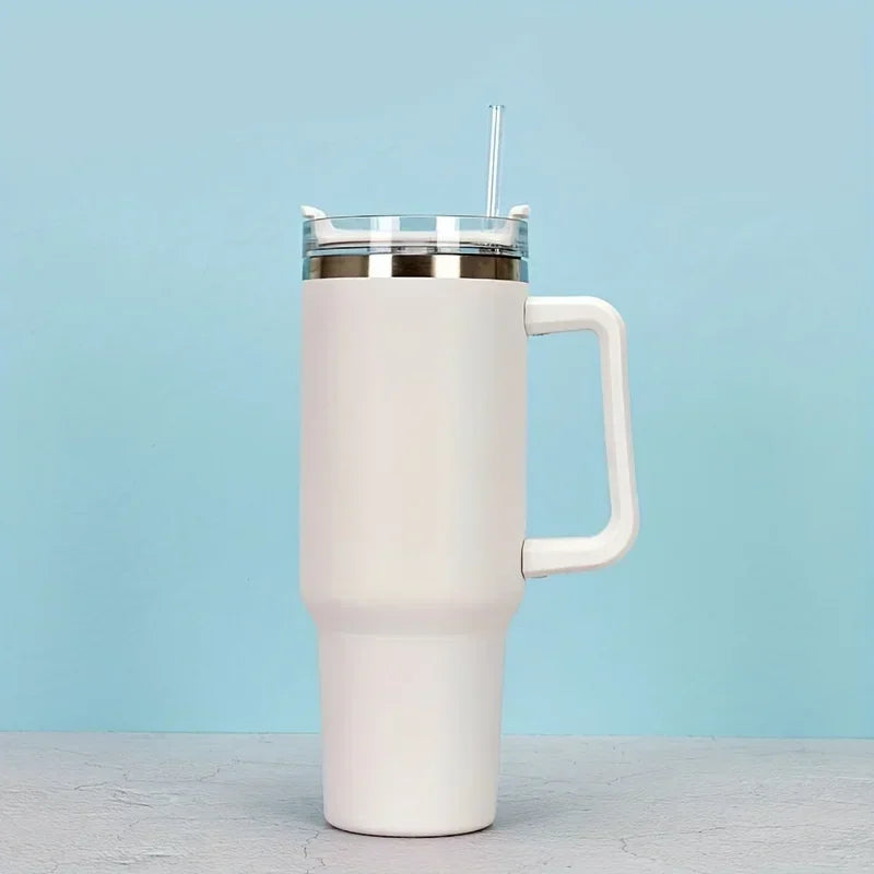 A white insulated stainless steel tumbler with a handle and straw is shown against a light blue background.