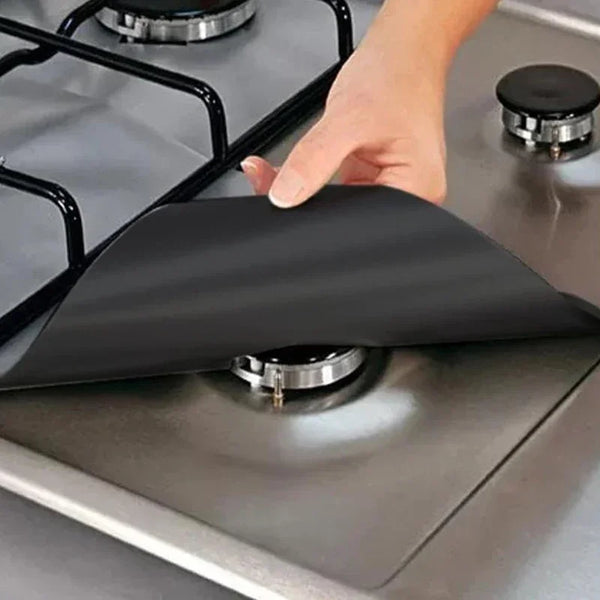 A hand places a black reusable gas stove burner protector onto a stovetop grate.