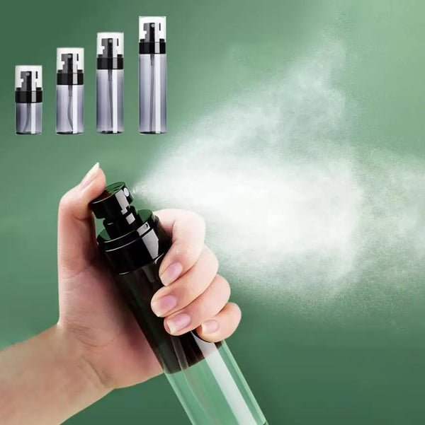A hand is spraying a clear glass bottle of refillable travel mist spray for skincare or cleaning onto a surface.