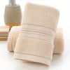 A beige ultra-absorbent pure cotton bath towel rolled and displayed next to a soap dispenser.