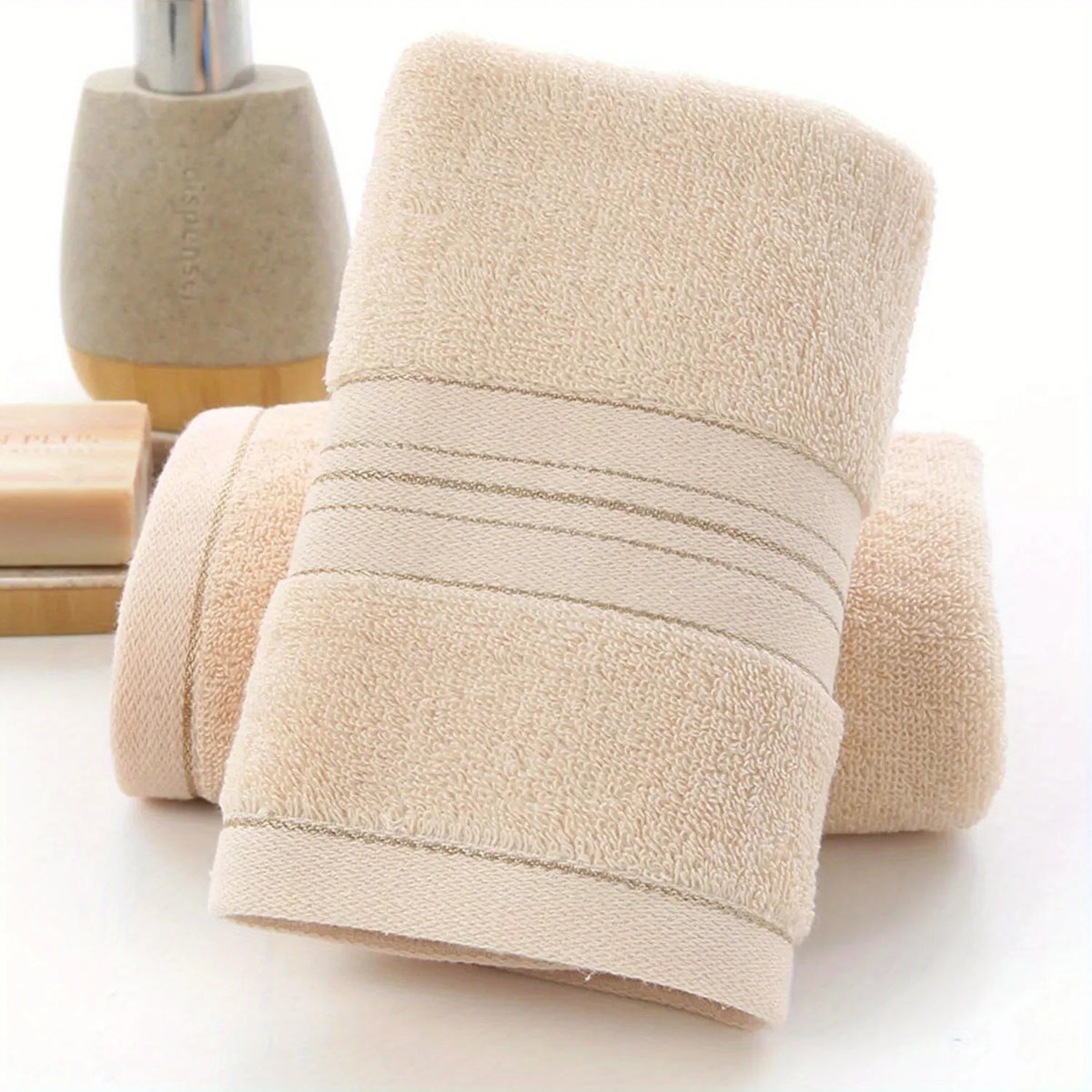A beige ultra-absorbent pure cotton bath towel rolled and displayed next to a soap dispenser.