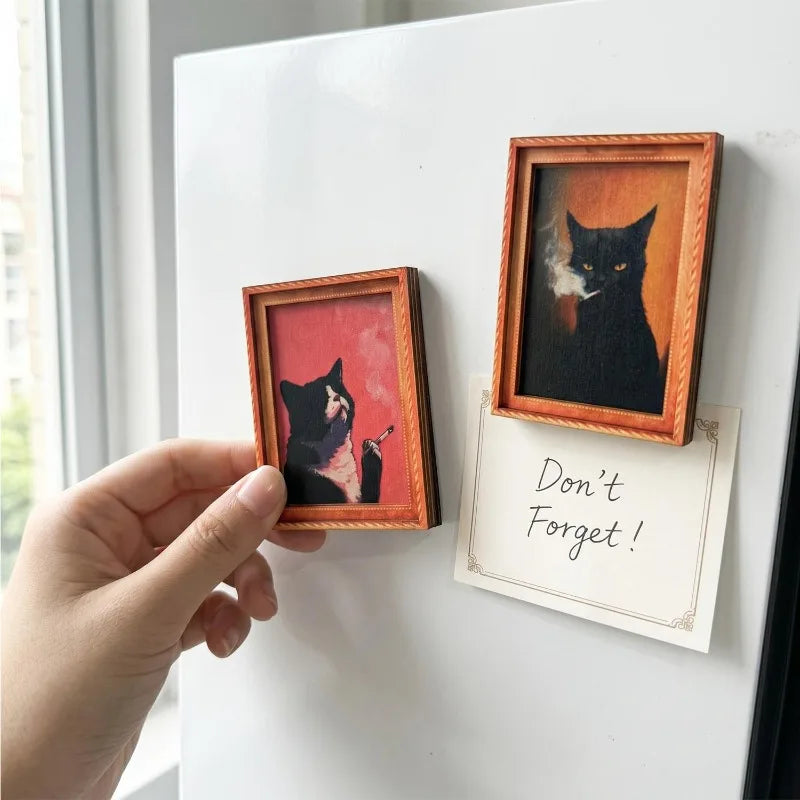 Eine Hand hält ein gerahmtes Bild einer schwarzen Katze mit leuchtenden Augen und Rauch auf einem weißen Kühlschrankmagnet.