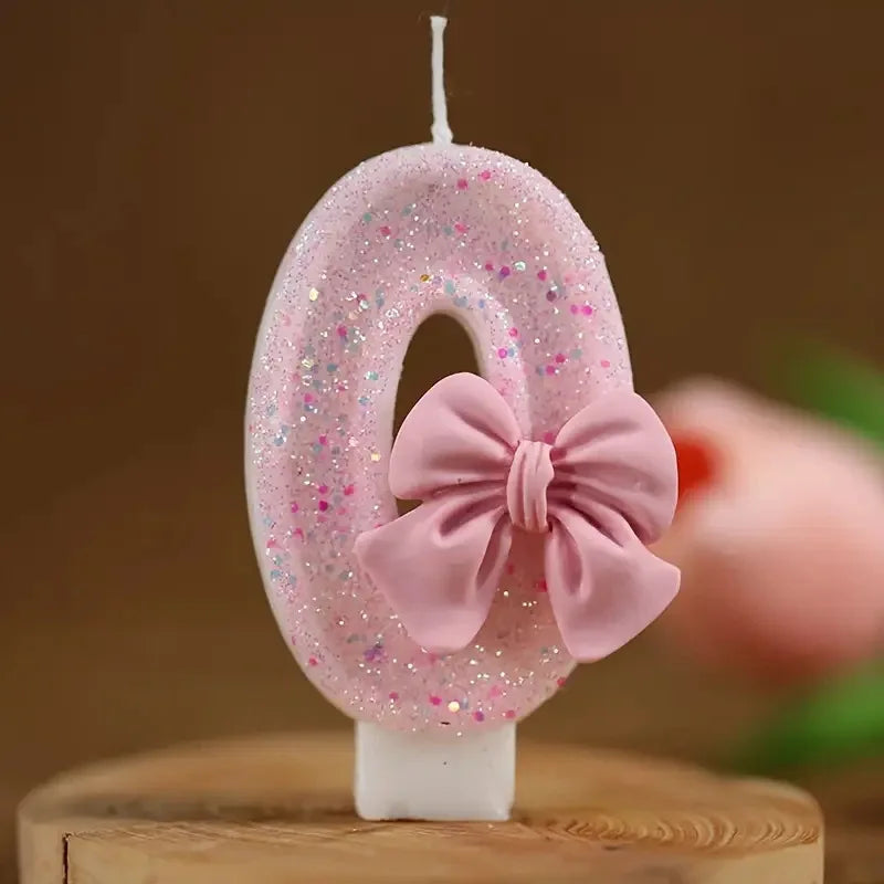A pink glitter number candle shaped like the number 6 with a pink bow on a white base.