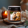 A dark glass jar candle with a custom photo insert showing a woman and a dog, resting on a wooden slice.
