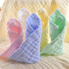 Ein Set aus drei gerollten, natürlichen Baumwoll-Muslin-Waschlappen in rosa, blau und grün auf einem gelben strukturierten St
