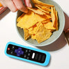 A hand is holding a bowl of yellow tortilla chips next to a blue silicone remote control cover.