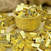 A golden cup filled with small rectangular gold bars and scattered pieces on a beige surface.