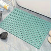 Una alfombra de ducha de PVC verde antideslizante con numerosos agujeros de drenaje sobre una superficie de azulejos grises.