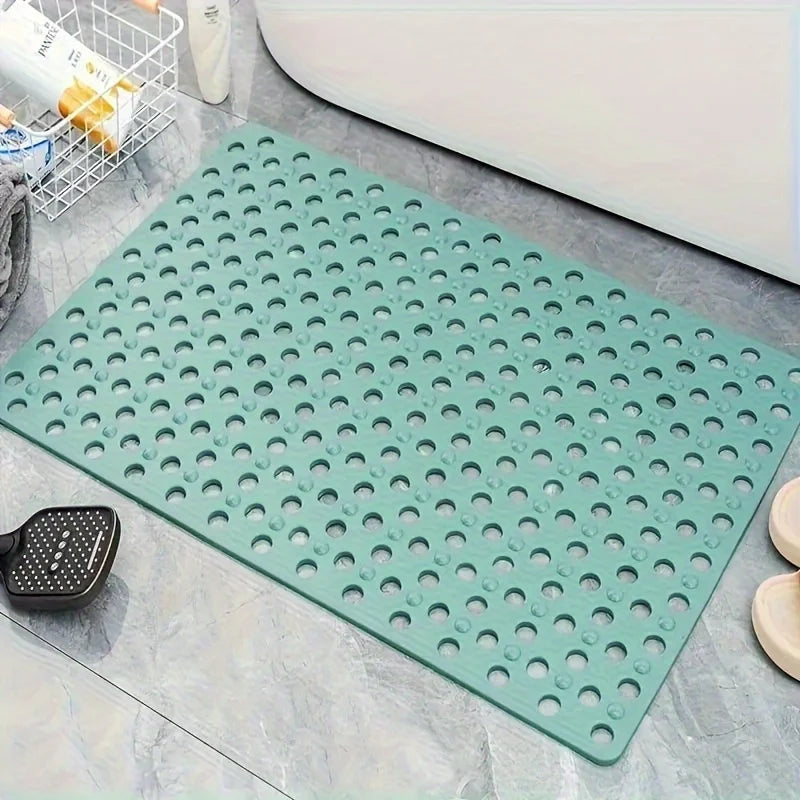 Una alfombra de ducha de PVC verde antideslizante con numerosos agujeros de drenaje sobre una superficie de azulejos grises.