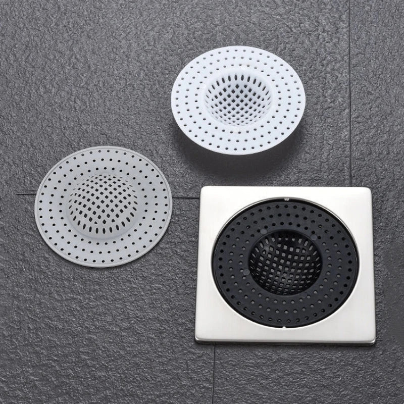 Three round metal drain strainers or hair catchers are displayed on a dark gray surface.