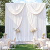 Fondo de tela blanca con cortinas drapeadas y arreglos florales para un evento.