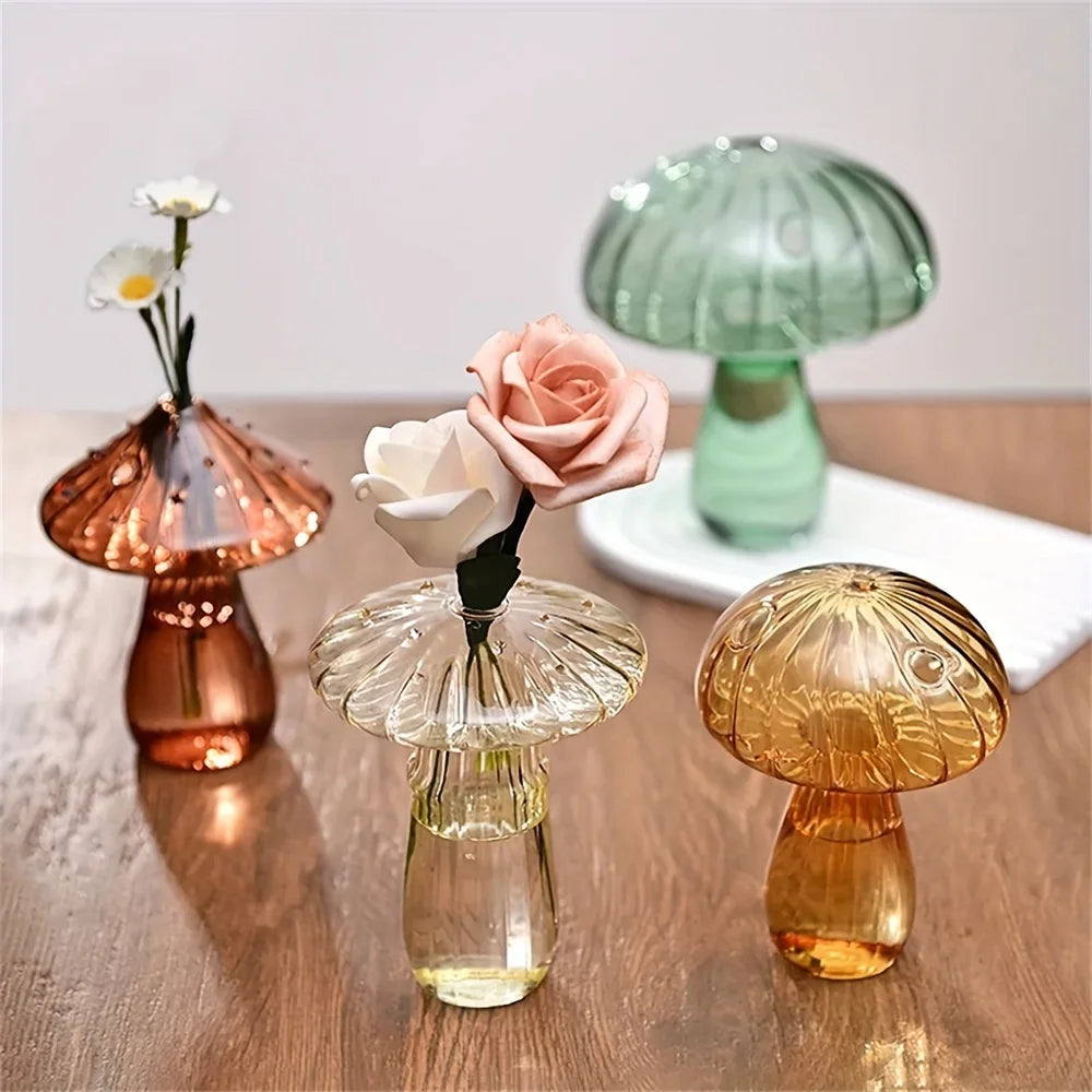 A set of three Nordic style glass mushroom vases in rose gold, clear, and amber tones on a wooden surface.
