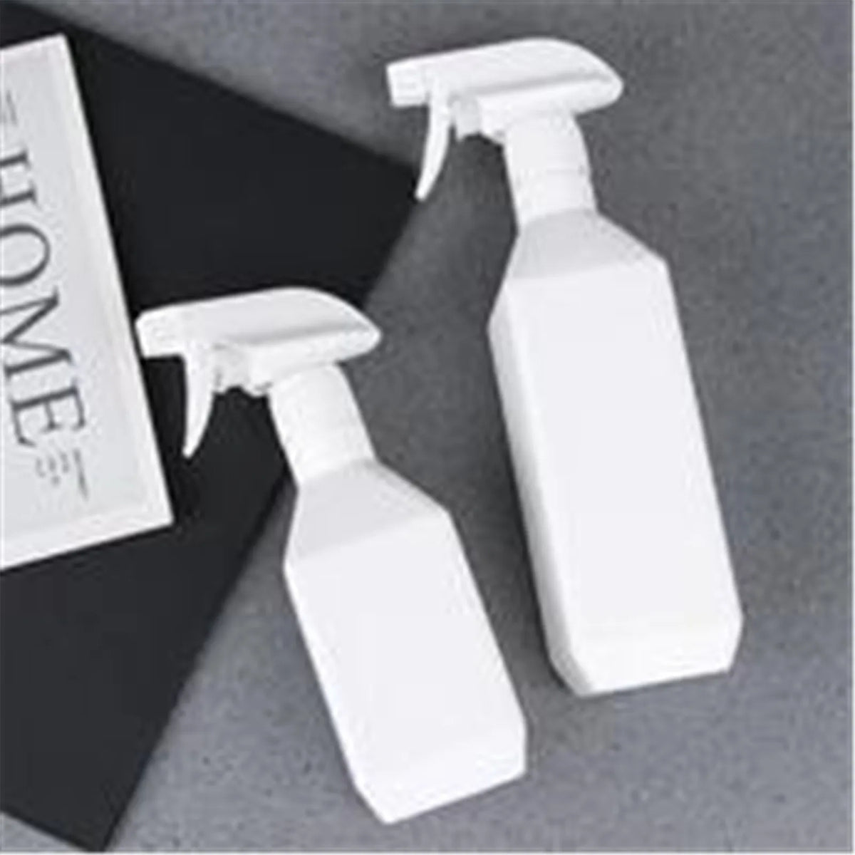 White refillable plastic spray bottles for plants and cleaning displayed on a dark surface.