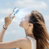 A woman uses an ice compress fan to direct cooling air onto her face outdoors.