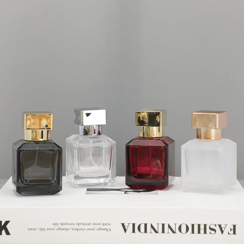 Four glass perfume bottles in various colors and finishes displayed on a white surface.