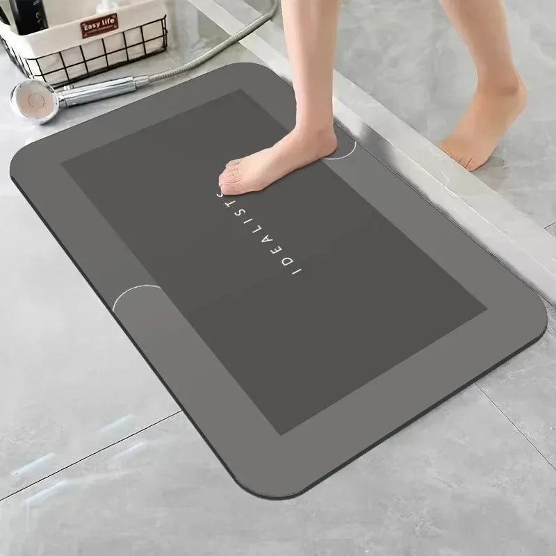 A gray diatomaceous earth absorbent bath mat is placed on a light gray floor next to a person's bare foot.