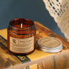 A brown glass jar candle labeled Aroma Sensation resting on a book.