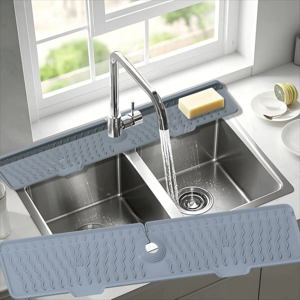 A silver kitchen sink with a silicone splash guard mat is shown under a window.