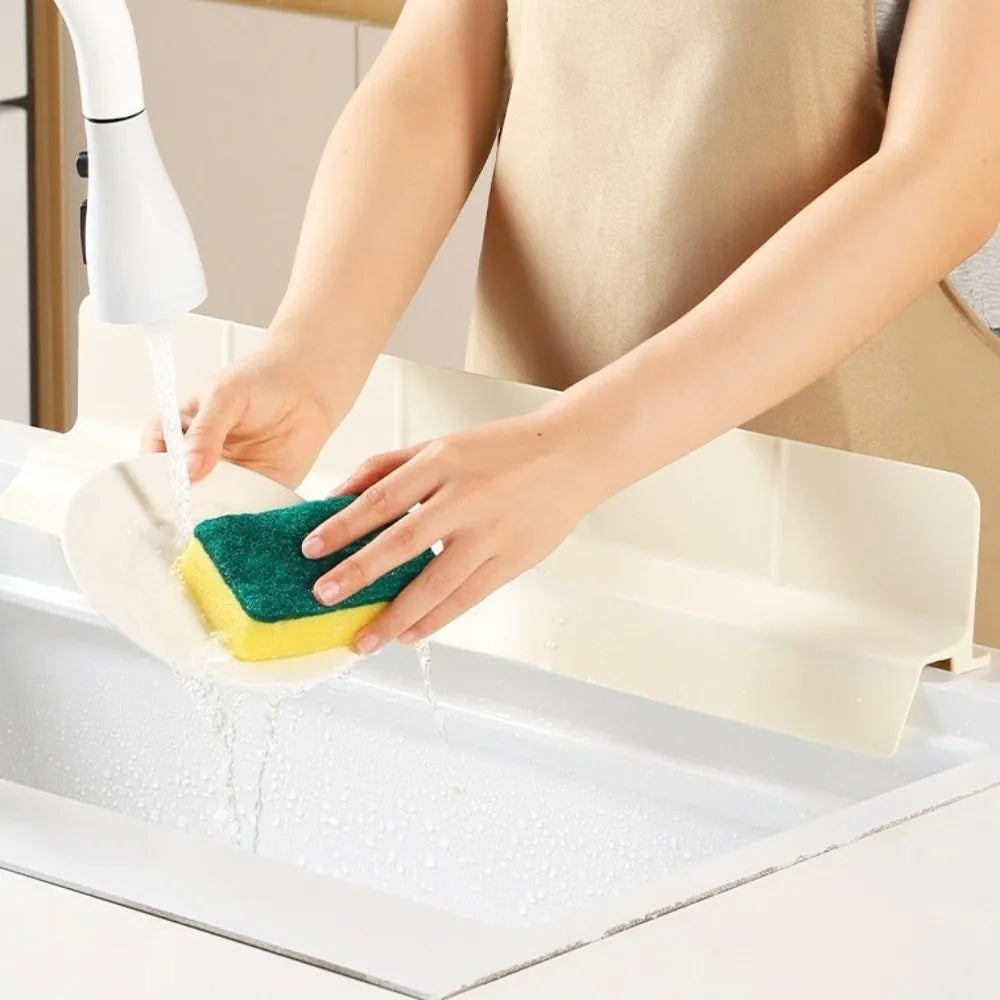 Eine Hand benutzt eine Silikon-Spüle, um eine Küchenspüle zu reinigen, mit Wasserfluss aus einem Wasserhahn.