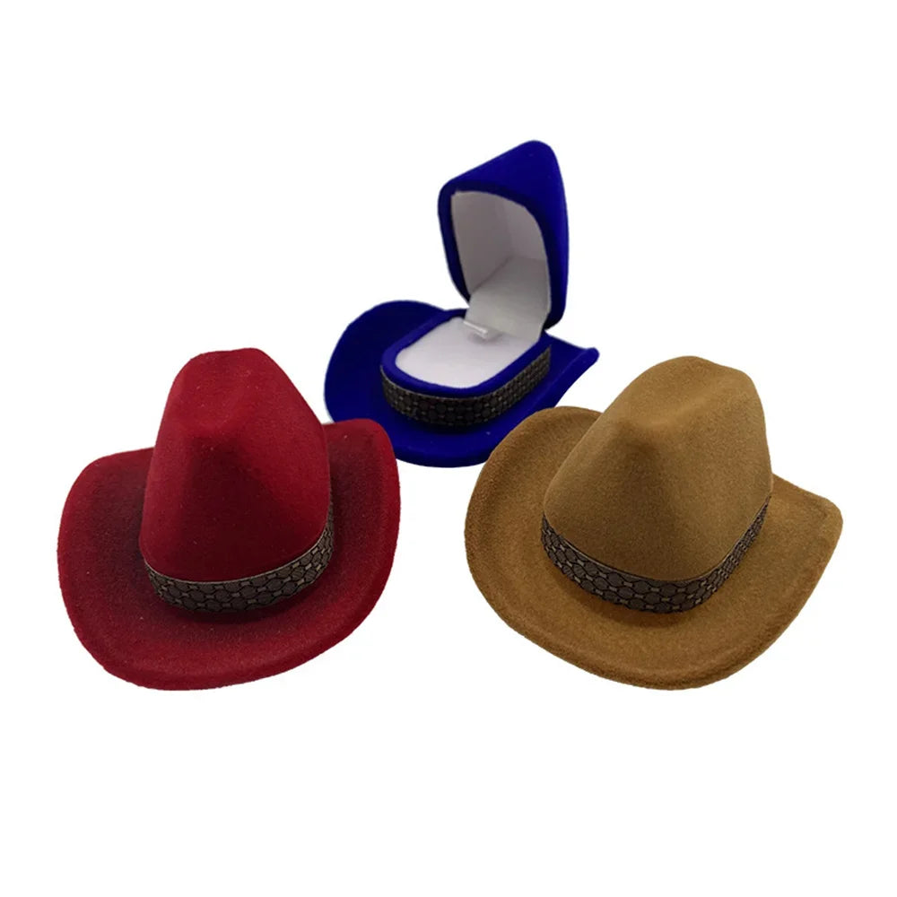 A velvet cowboy hat is displayed next to a brown felt cowboy hat and a blue jewelry storage box.