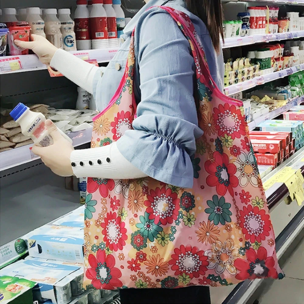 Eine Person hält eine rosa Blumen-Mehrwegtasche beim Einkaufen in einem Supermarktgang.