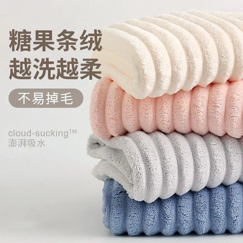 Ein Stapel flauschiger Samt-Handtücher in verschiedenen Pastellfarben wie Rosa, Creme, Grau und Blau.