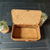 Handwoven rattan storage basket with a lid shown open on a dark wooden surface.