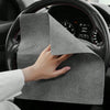 A hand is holding a gray reusable microfiber cleaning cloth on the steering wheel of a car.