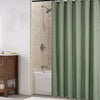 A vertical shot of a sage green waterproof shower curtain hanging in a bathroom with a tiled shower and a wooden cabinet.