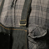 Close-up of a dark gray plaid denim tool apron with a leather buckle and pocket on the chest.
