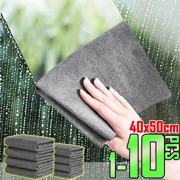 A hand is holding a gray microfiber glass cleaning cloth against a green leaf background.
