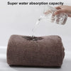 A hand pours water onto a thick, brown bath wrap towel demonstrating its super water absorption capacity.