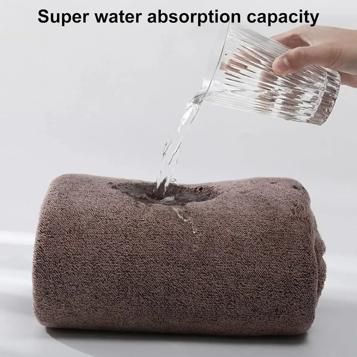 A hand pours water onto a thick, brown bath wrap towel demonstrating its super water absorption capacity.