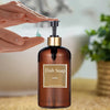 A hand is dispensing liquid dish soap from a pump dispenser bottle with a gold top into the air.