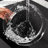 A hand is pouring liquid into a clear glass bowl, demonstrating the splatter guard feature.