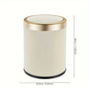 A cylindrical trash can with a gold rim and cream-colored ribbed body.