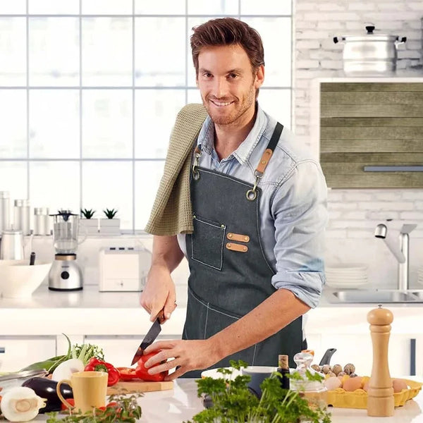 A man wearing a dark canvas cooking apron is preparing food in a bright kitchen setting.