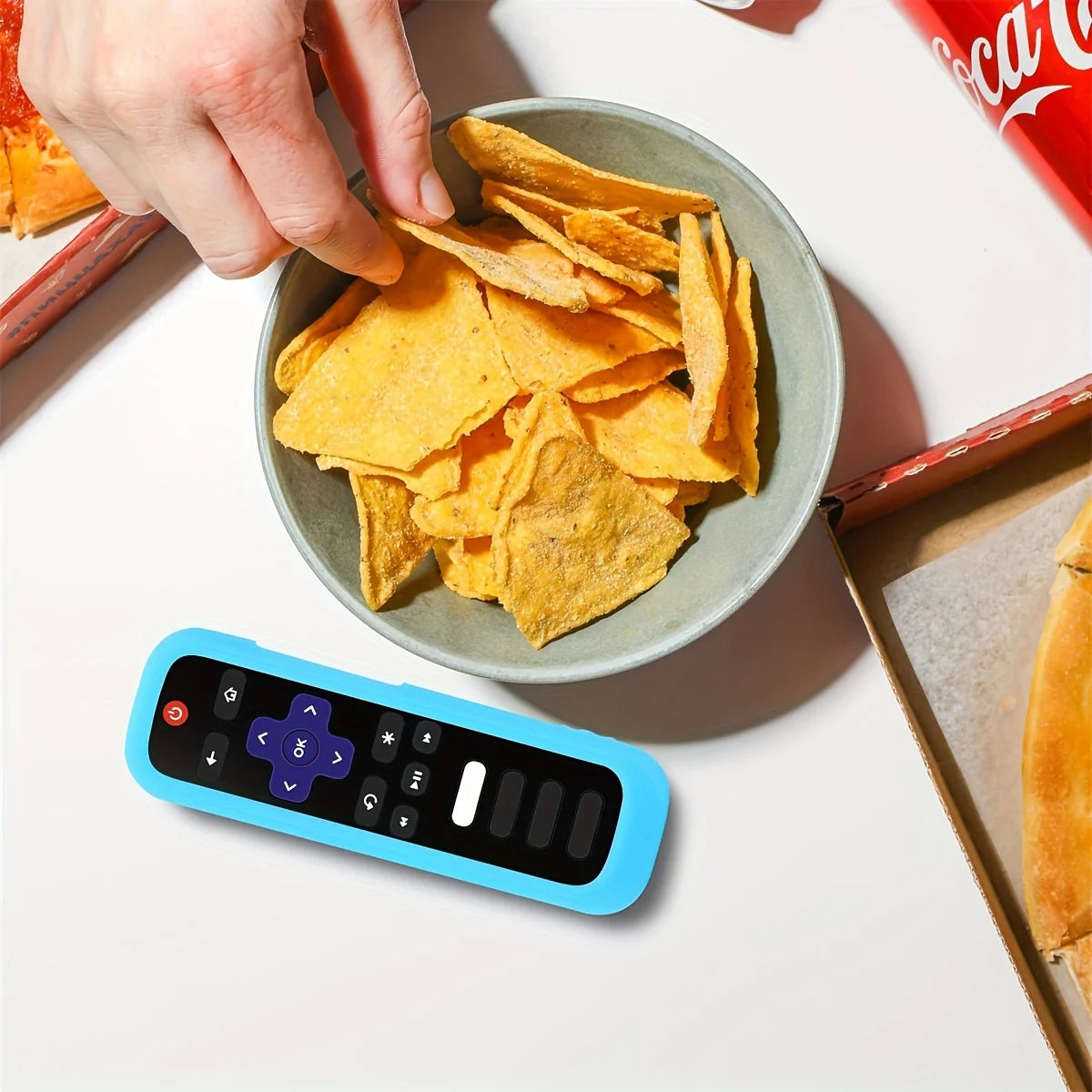 A hand holds a glow-in-the-dark silicone remote control cover with a lanyard next to tortilla chips.